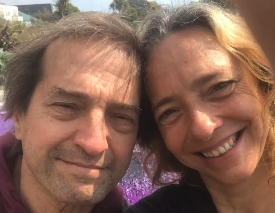 Two people smiling and taking a close-up selfie outdoors with sunlight on their faces.