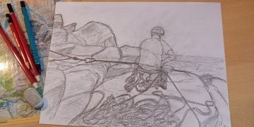 A pencil sketch shows a rock climber with ropes and gear from behind, placed on a wooden desk surrounded by art supplies.