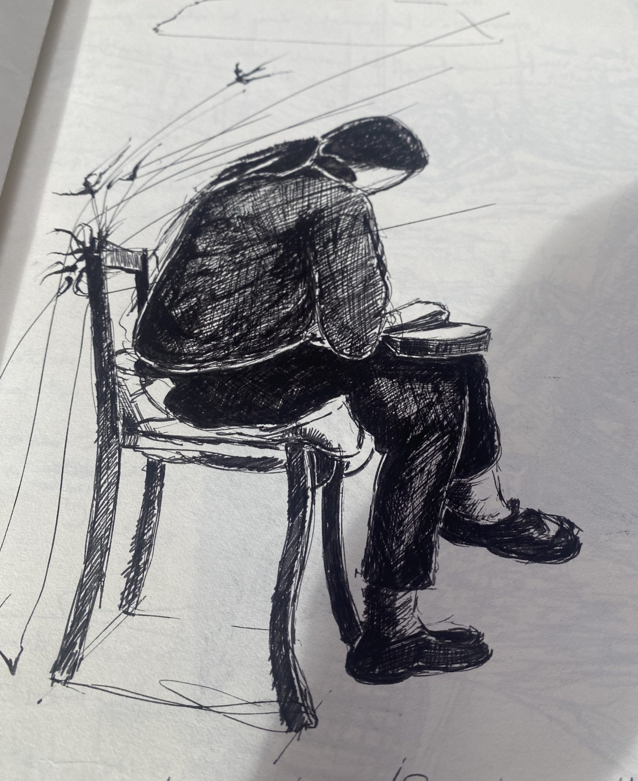 Black ink drawing of a person hunched over on a chair, focused on writing or sketching in a notebook.